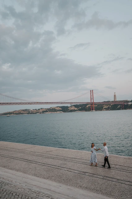 The couple beneath an open evening sky | Lisbon couple photoshoot The couple holding hands beside the river with open water and clouds filling the view during their couple photoshoot in Lisbon.