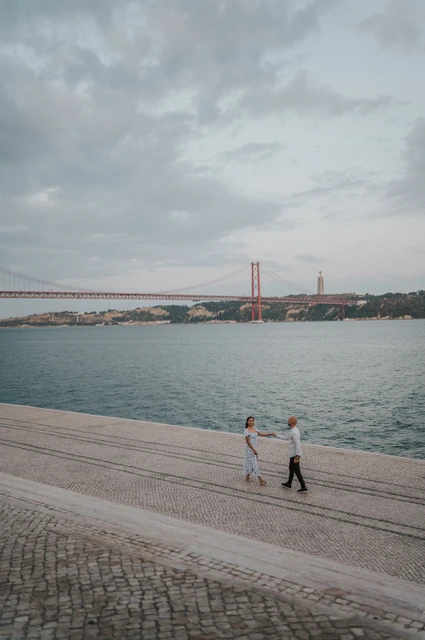 An evening portrait from above | Lisbon couple photoshoot An elevated view of the couple holding hands beside the river beneath an evening sky during their couple photoshoot in Lisbon.