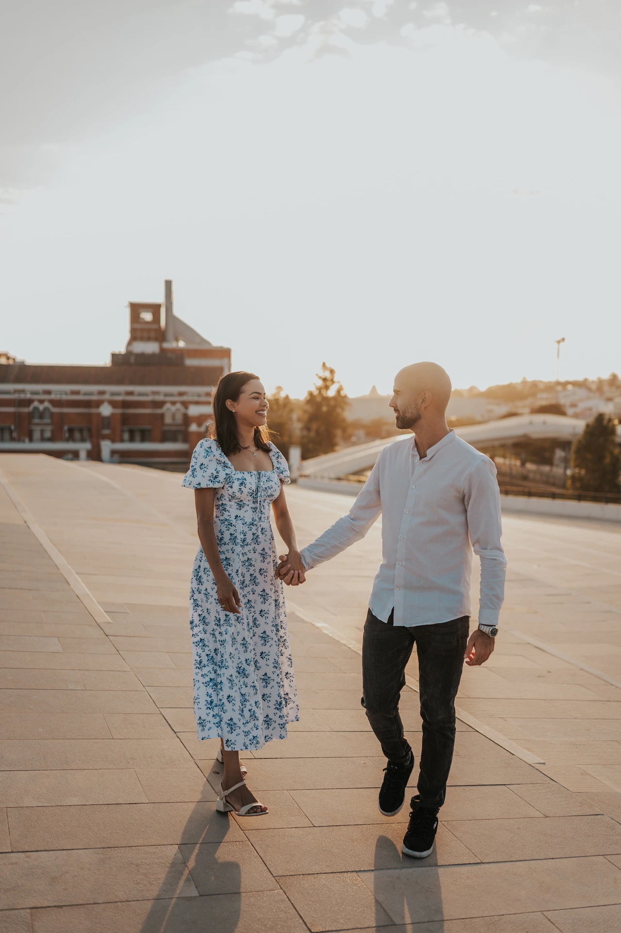 The couple holding hands and looking at each other on the MAAT plaza during their couple photoshoot in Lisbon.