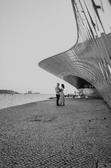 The curved MAAT facade in black and white | Lisbon couple photoshoot A black-and-white distant portrait of the couple beneath the curved MAAT facade during their couple photoshoot in Lisbon.