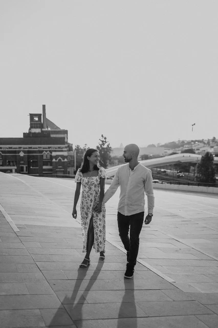 A plaza walk in black and white | Lisbon couple photoshoot A black-and-white portrait of the couple walking hand in hand across the MAAT plaza during their couple photoshoot in Lisbon.