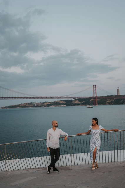 A shared glance at the river railing | Lisbon couple photoshoot The couple leaning against the railing above the river and looking at each other during their couple photoshoot in Lisbon.