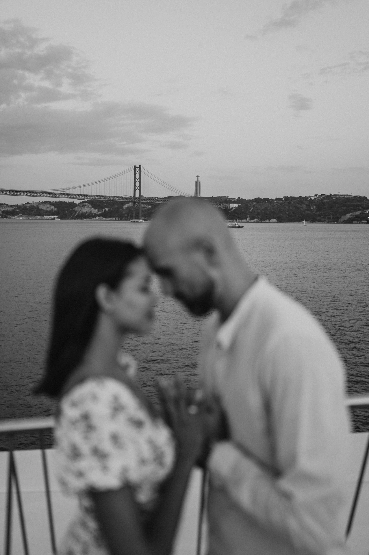 A softly focused black-and-white portrait of the couple leaning together at the river railing during their couple photoshoot in Lisbon.