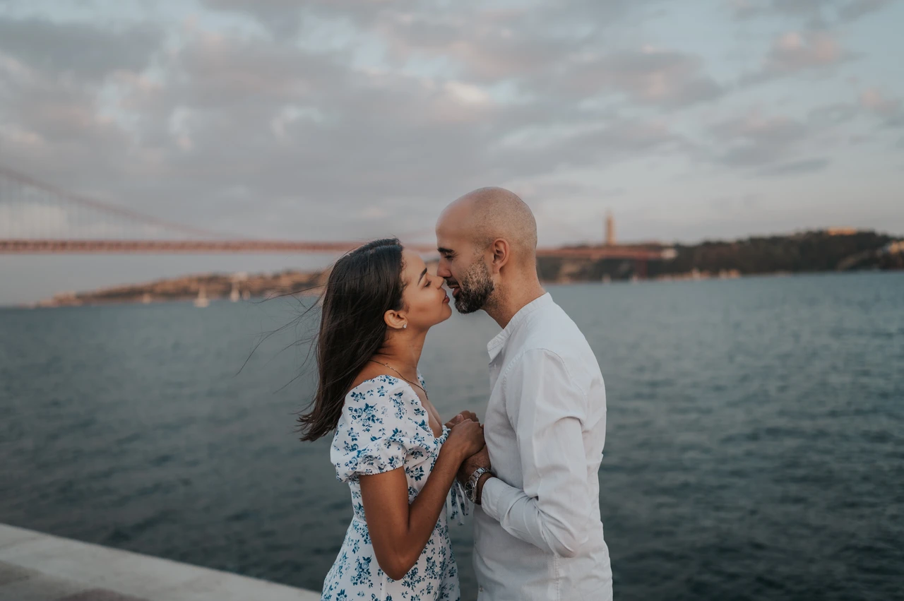 A close kiss beside the water | Lisbon couple photoshoot A close kiss beside the water, with the 25 de Abril Bridge in the background during their couple photoshoot in Lisbon.