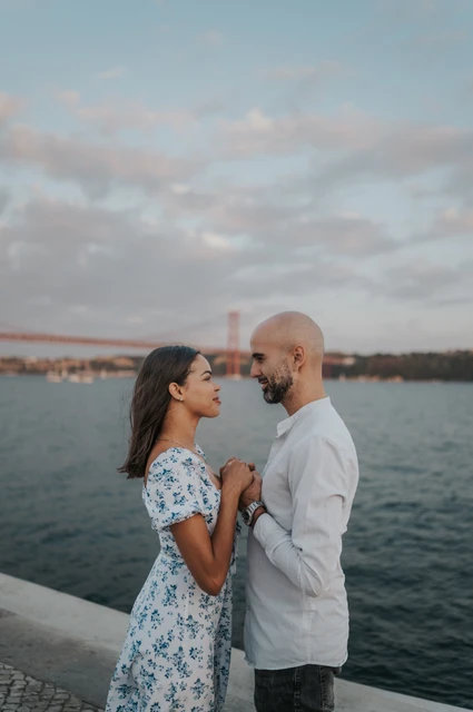 A close moment beside the river | Lisbon couple photoshoot The couple facing each other and holding hands close to their chests beside the river during their couple photoshoot in Lisbon.