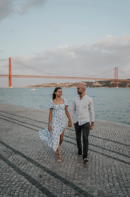 A floral dress on the riverfront | Lisbon couple photoshoot The woman’s floral dress moving as the couple walk along the cobbled waterfront during their couple photoshoot in Lisbon.