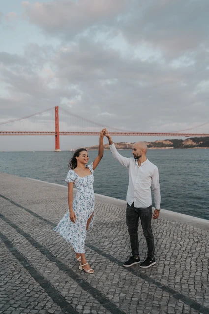Joined hands above the riverfront | Lisbon couple photoshoot The couple raising their joined hands for a turn beside the river and bridge during their couple photoshoot in Lisbon.