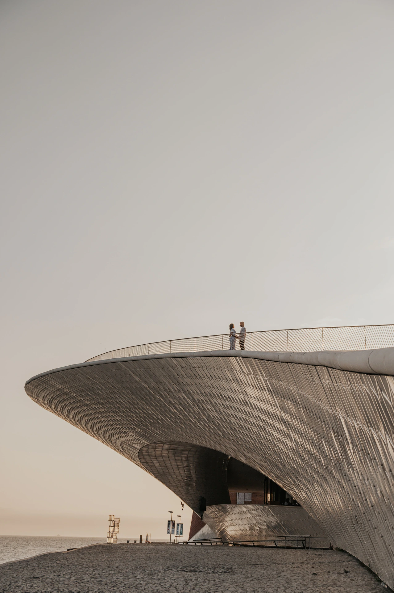 A distant view of the couple on the curved roof of the MAAT beside the water during their couple photoshoot in Lisbon.
