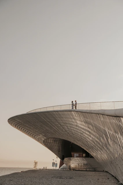 A distant portrait on the MAAT roof | Lisbon couple photoshoot A distant view of the couple on the curved roof of the MAAT beside the water during their couple photoshoot in Lisbon.