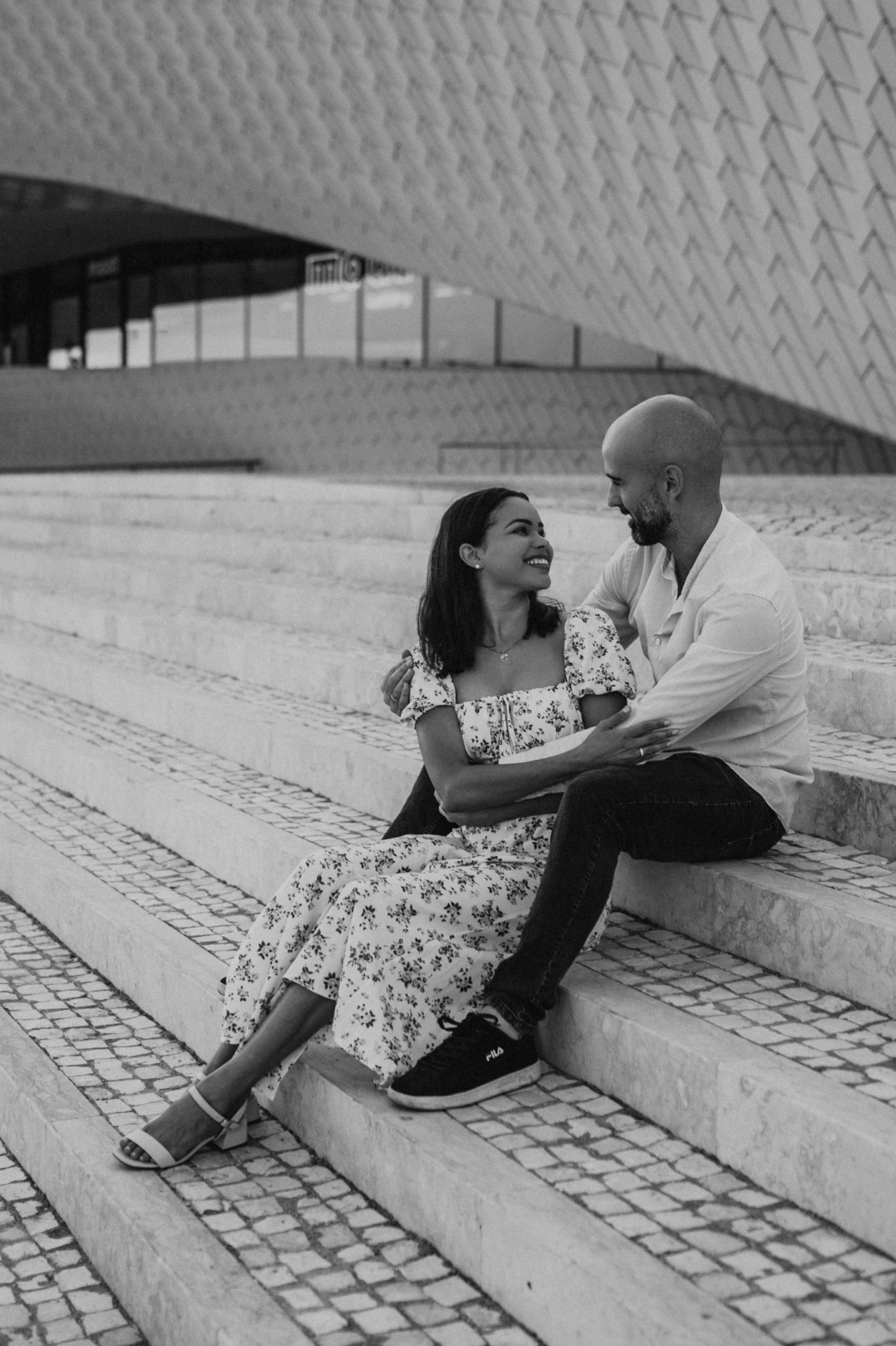 A black-and-white portrait of the couple smiling at each other on the MAAT steps during their couple photoshoot in Lisbon.