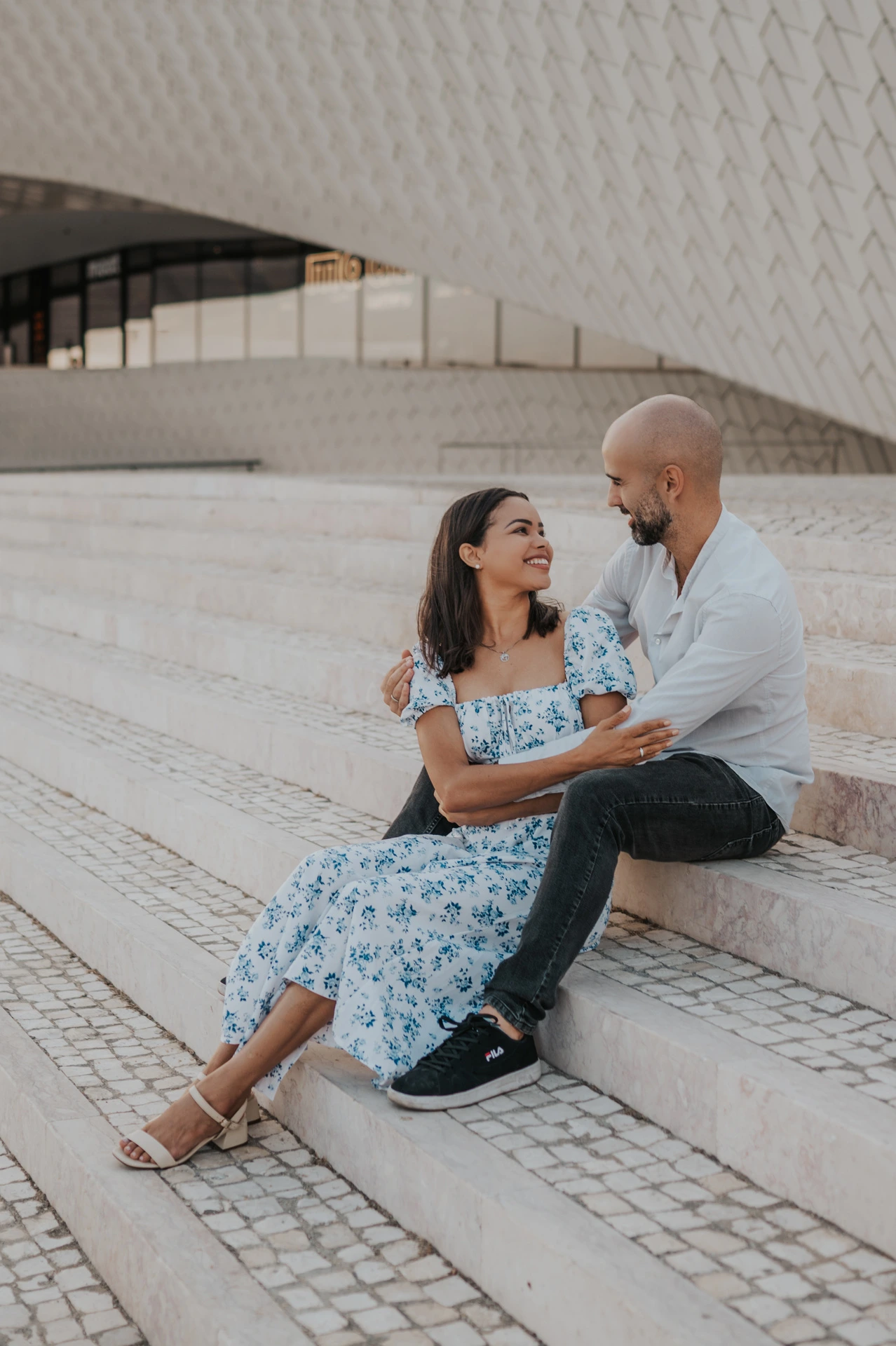 A closer portrait of the couple sitting together beneath the tiled MAAT facade during their couple photoshoot in Lisbon.