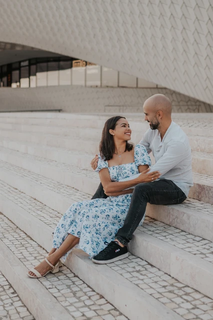 A closer portrait of the couple sitting together beneath the tiled MAAT facade during their couple photoshoot in Lisbon.