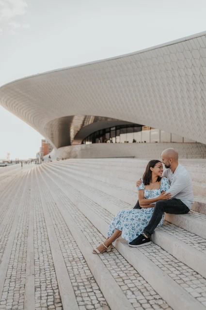 The MAAT curve around a seated couple | Lisbon couple photoshoot The couple seated on the steps with the curved MAAT building rising behind them during their couple photoshoot in Lisbon.