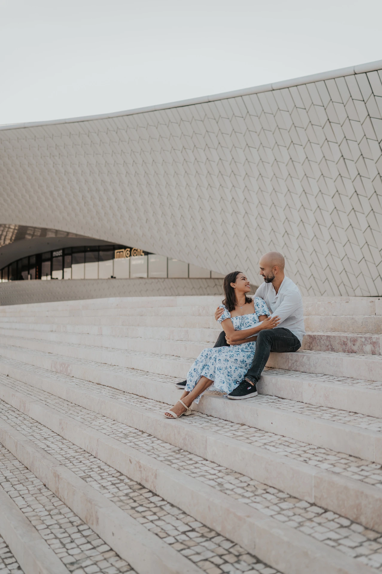 The seated couple turning towards each other on the MAAT steps during their couple photoshoot in Lisbon.