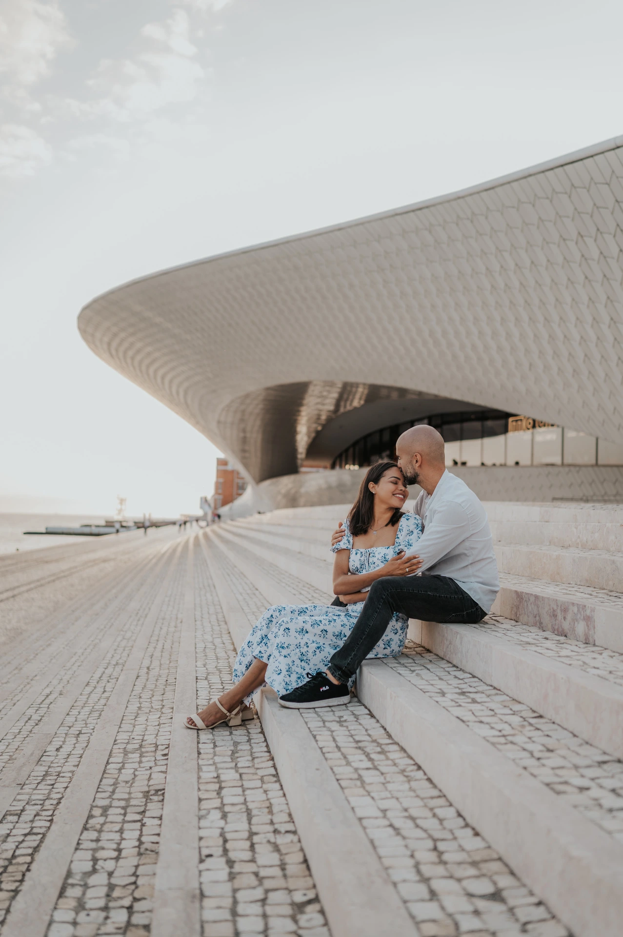 A forehead kiss while the couple sit on the steps outside the MAAT during their couple photoshoot in Lisbon.