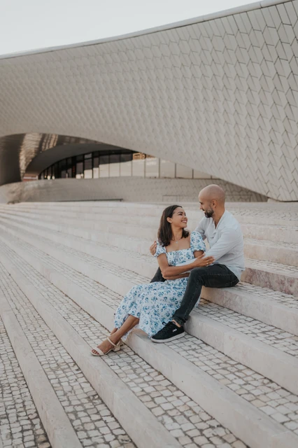 A smile together on the MAAT steps | Lisbon couple photoshoot The woman smiling up at her partner as they sit together on the MAAT steps during their couple photoshoot in Lisbon.