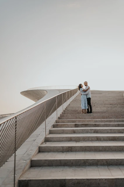 An embrace at the top of the MAAT steps | Lisbon couple photoshoot The couple embracing at the top of the MAAT staircase beside the curved railing during their couple photoshoot in Lisbon.