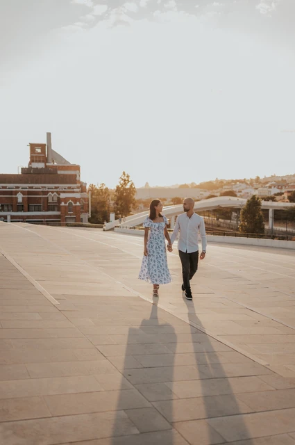 Walking together across the MAAT plaza | Lisbon couple photoshoot The couple walking hand in hand across the MAAT plaza, with long shadows in front of them during their couple photoshoot in Lisbon.