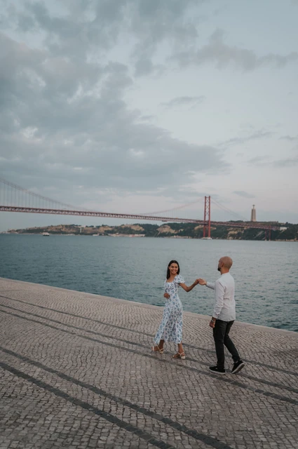 Together against the river and bridge | Lisbon couple photoshoot The couple holding hands with the river and bridge stretching out behind them during their couple photoshoot in Lisbon.