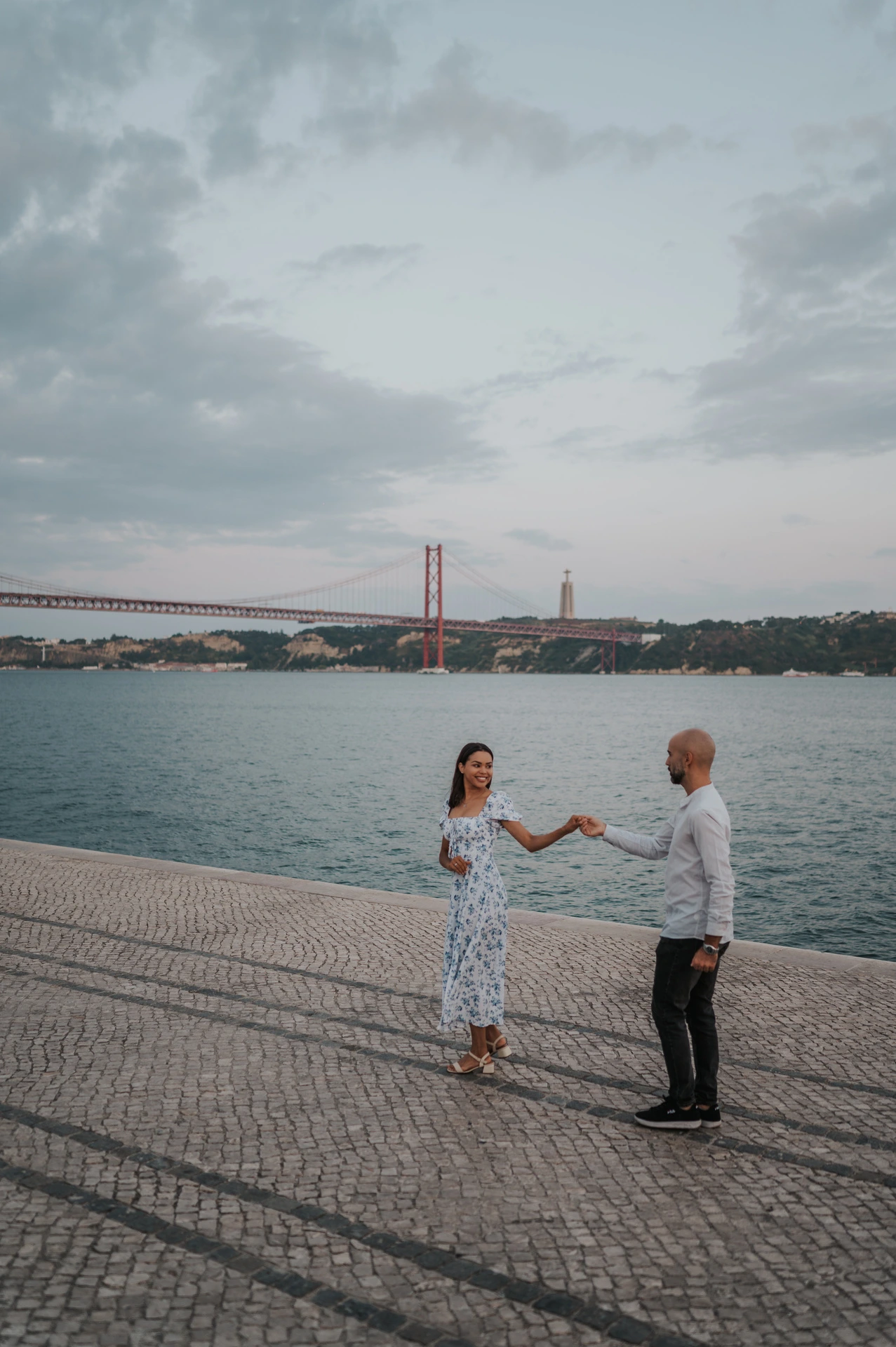 The couple standing apart with their hands joined on the cobbled waterfront during their couple photoshoot in Lisbon.