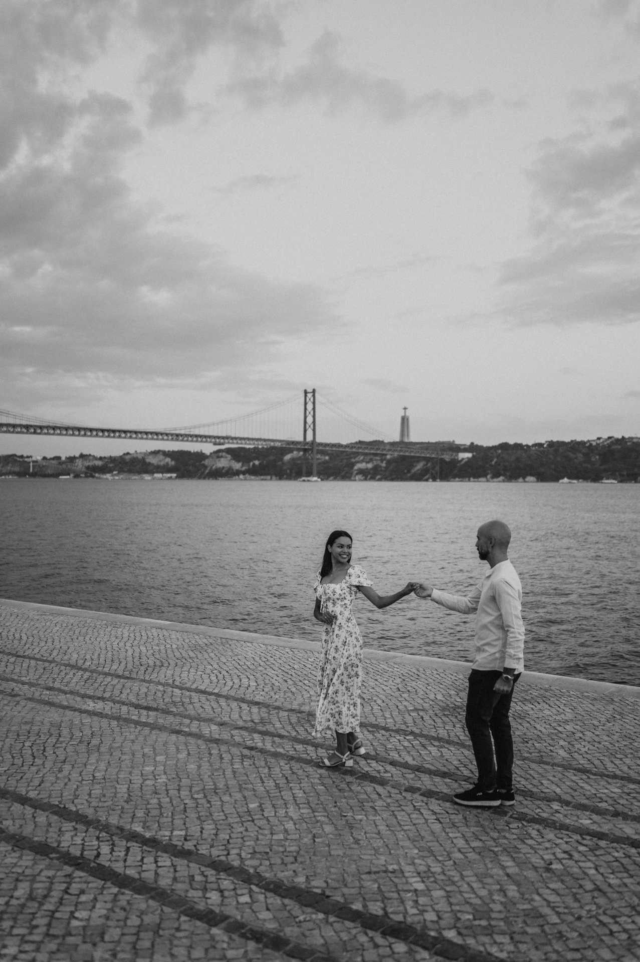 A black-and-white portrait of the couple reaching towards each other beside the river during their couple photoshoot in Lisbon.