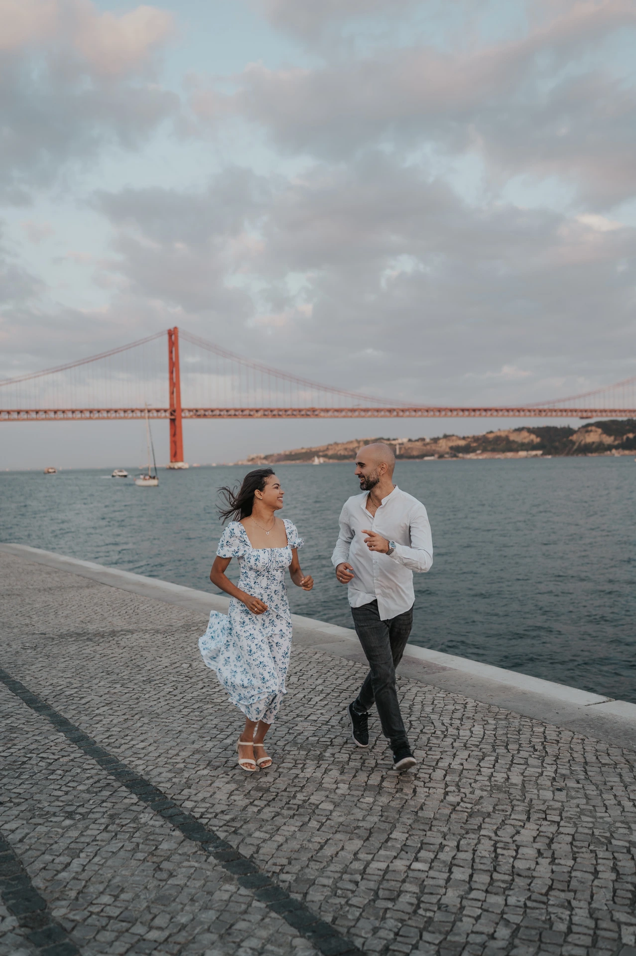 The couple taking lively steps together along the cobbled waterfront during their couple photoshoot in Lisbon.
