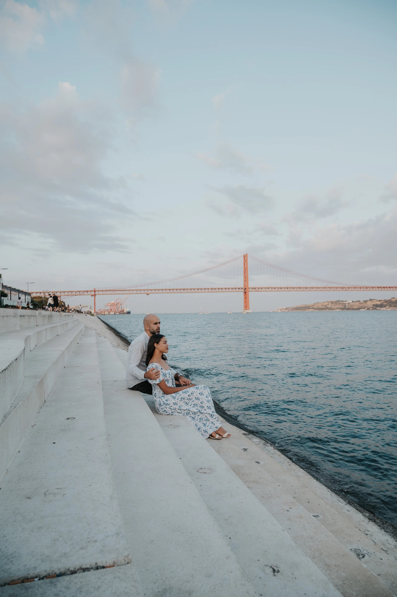 The couple embracing while seated on the steps beside the river during their couple photoshoot in Lisbon.