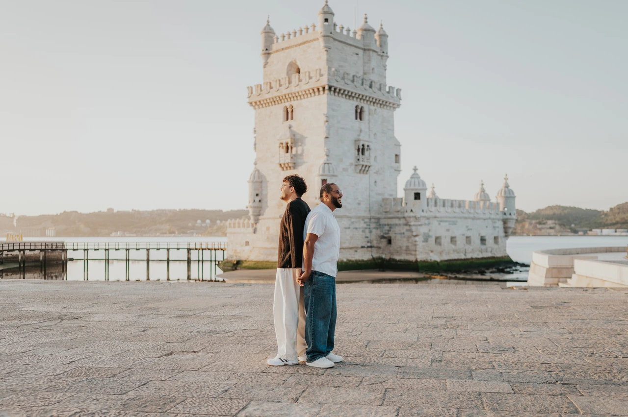 A back-to-back waterfront portrait | Lisbon couple photoshoot A landscape view of the couple standing back to back with Belém Tower behind them during their couple photoshoot in Lisbon.