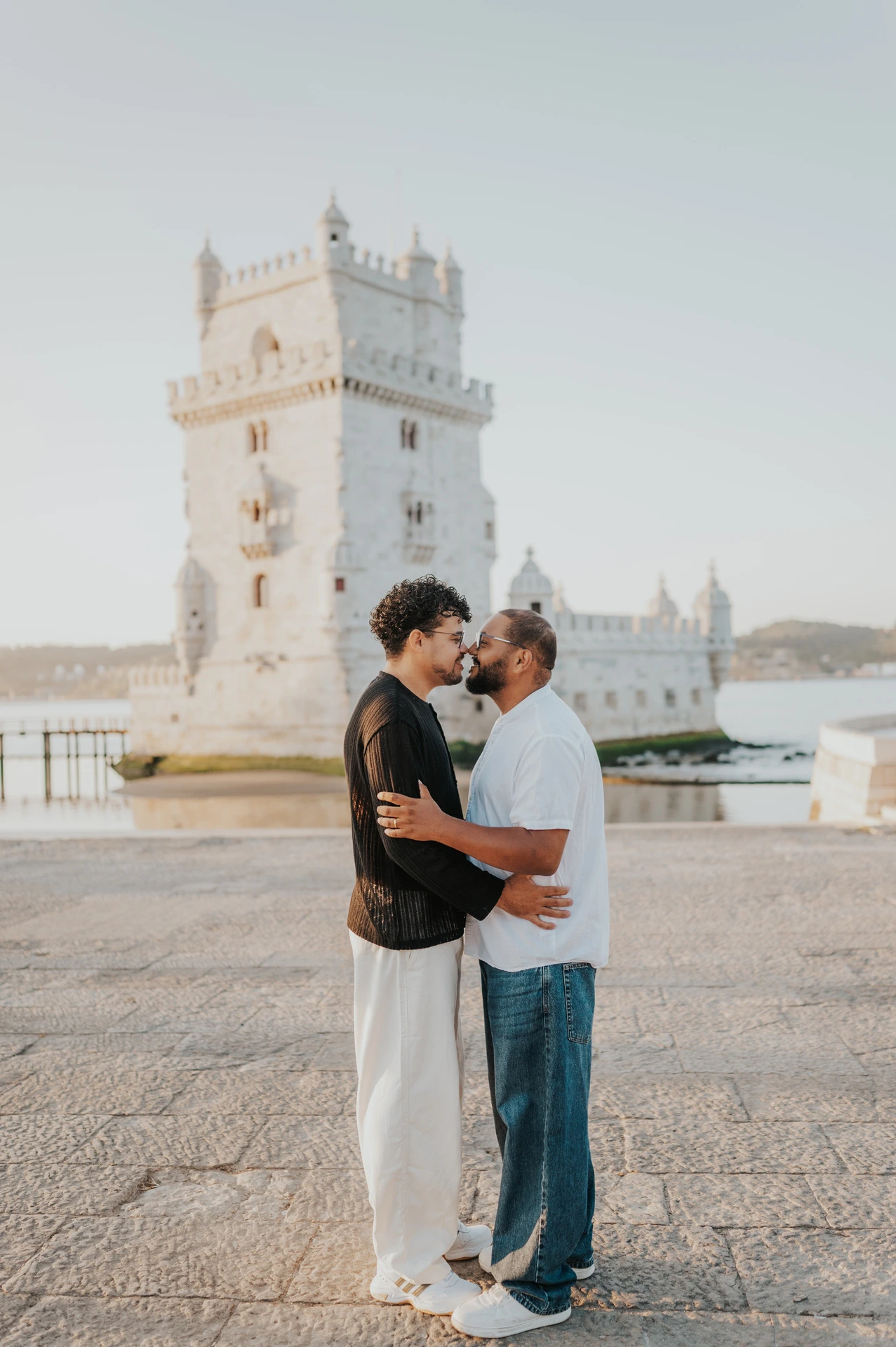 The couple kissing while holding each other beside Belém Tower during their couple photoshoot in Lisbon.