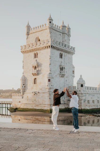 The couple raising their joined hands between them with Belém Tower behind them during their couple photoshoot in Lisbon.