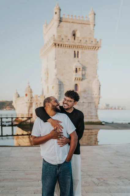 A cheek kiss beside Belém Tower | Lisbon couple photoshoot One partner kissing the other on the cheek while embracing him from behind at Belém Tower during their couple photoshoot in Lisbon.