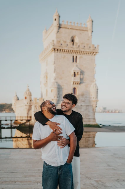 A shared smile in an embrace | Lisbon couple photoshoot The couple looking at each other and smiling in an embrace with Belém Tower behind them during their couple photoshoot in Lisbon.