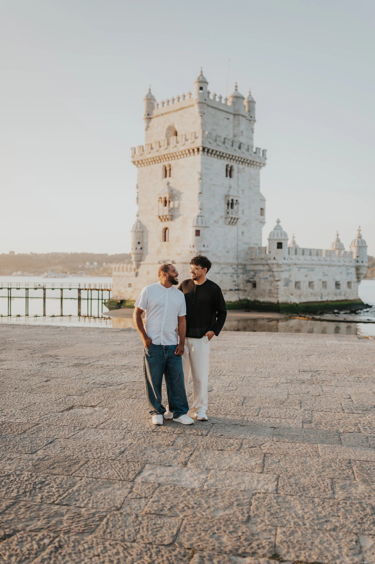 The couple standing close together with an arm around a shoulder beside Belém Tower during their couple photoshoot in Lisbon.
