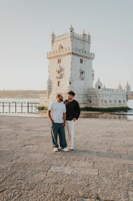 A shared glance beneath the tower | Lisbon couple photoshoot The couple standing close together with an arm around a shoulder beside Belém Tower during their couple photoshoot in Lisbon.