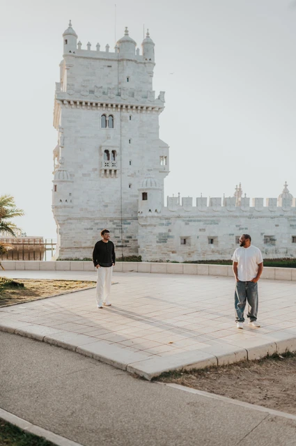 A wide portrait on the waterfront | Lisbon couple photoshoot The couple standing apart on the waterfront paving with Belém Tower behind them during their couple photoshoot in Lisbon.