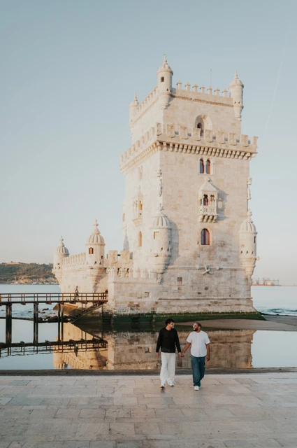 Walking together beside Belém Tower | Lisbon couple photoshoot The couple walking towards the camera with Belém Tower and the water behind them during their couple photoshoot in Lisbon.