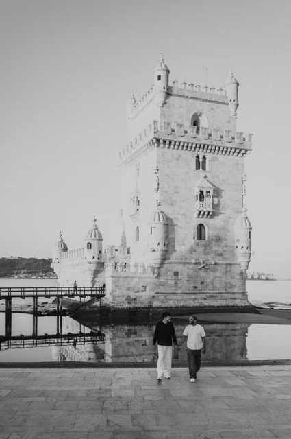 A tower walk in black and white | Lisbon couple photoshoot A black-and-white photograph of the couple walking hand in hand in front of Belém Tower during their couple photoshoot in Lisbon.