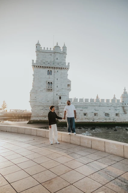 A portrait at the low waterfront wall | Lisbon couple photoshoot A wider portrait of the couple standing at different levels by the low stone wall in front of Belém Tower during their couple photoshoot in Lisbon.