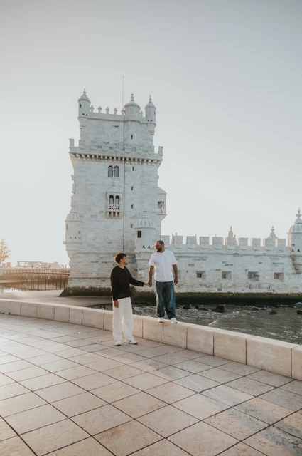 Joined hands across the stone ledge | Lisbon couple photoshoot The couple holding hands while standing at different levels beside the low wall at Belém Tower during their couple photoshoot in Lisbon.