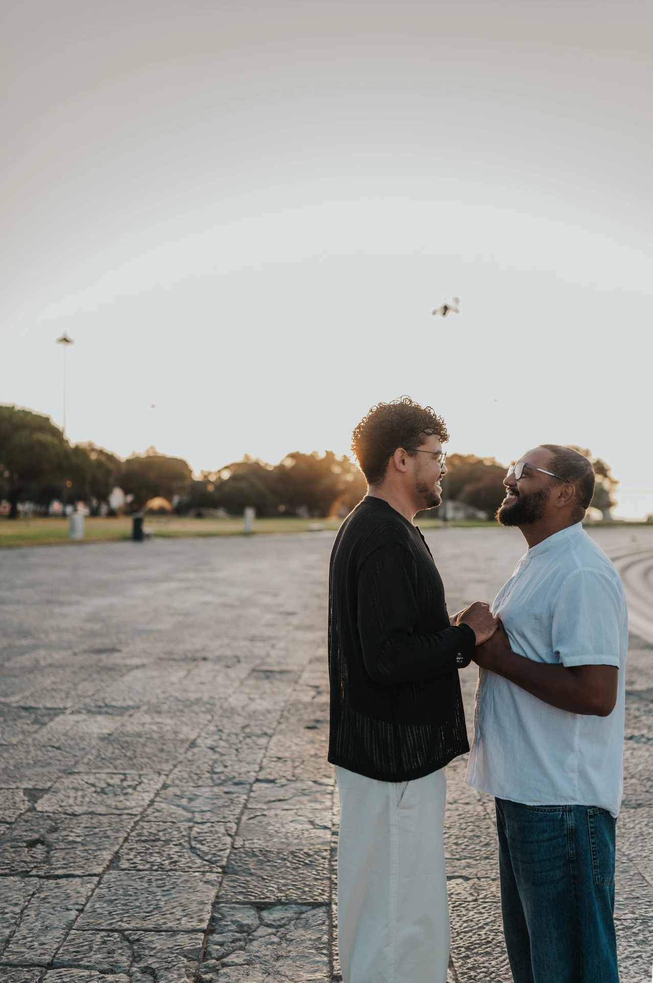 The couple facing each other and holding hands with the morning sun behind them on the waterfront during their couple photoshoot in Lisbon.