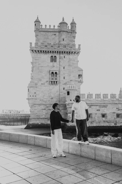 A hand-in-hand ledge portrait in black and white | Lisbon couple photoshoot A black-and-white photograph of the couple holding hands across the low waterfront ledge by Belém Tower during their couple photoshoot in Lisbon.
