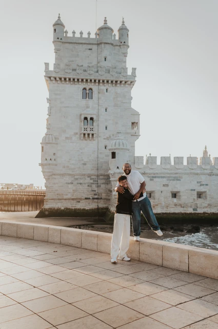A laughing lift beside Belém Tower | Lisbon couple photoshoot One partner lifting the other into a laughing embrace in front of Belém Tower during their couple photoshoot in Lisbon.