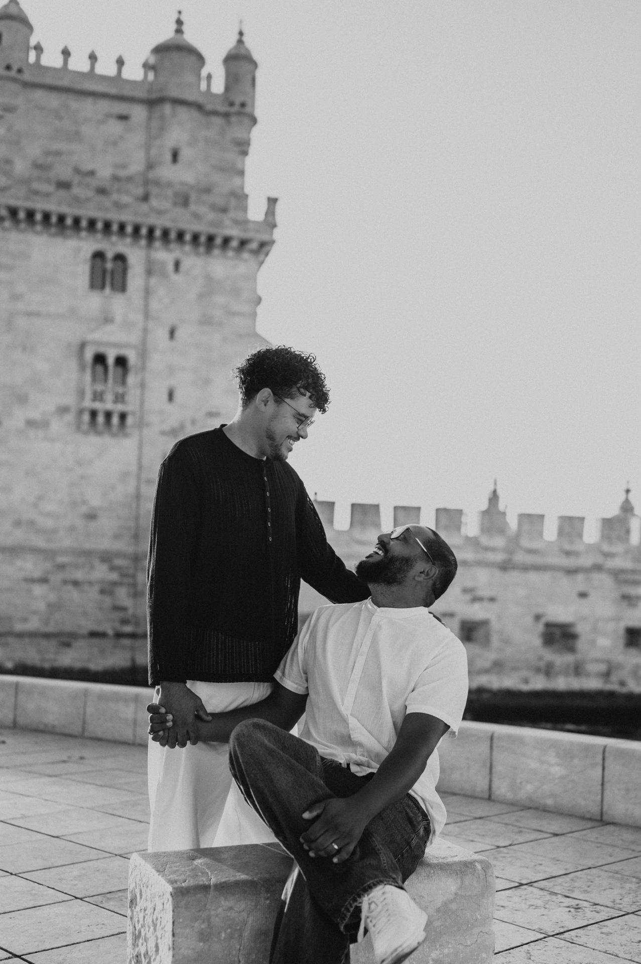 A black-and-white portrait of one partner seated and looking up at the other beside Belém Tower during their couple photoshoot in Lisbon.