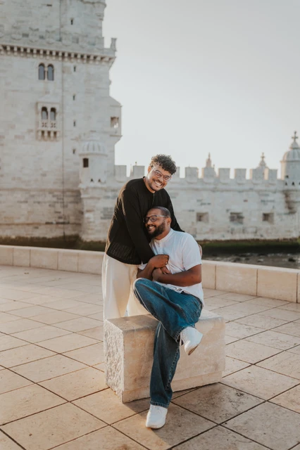 An embrace beside the waterfront ledge | Lisbon couple photoshoot The seated partner leaning into the other for an embrace by the stone waterfront ledge during their couple photoshoot in Lisbon.