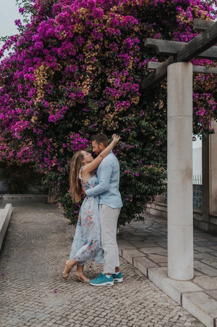 The man lifting his partner in an embrace beside bright flowers at Santa Luzia during their couple photoshoot in Lisbon.