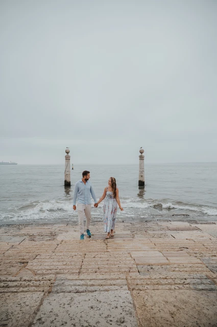 Joined hands at the waterfront | Lisbon couple photoshoot The couple standing apart with hands joined on the waterfront steps near Praça do Comércio during their couple photoshoot in Lisbon.