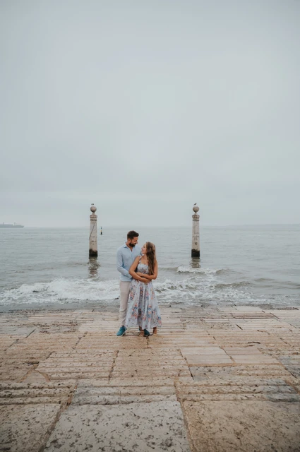 A kiss by the river | Lisbon couple photoshoot The couple sharing a kiss with the river and stone columns behind them near Praça do Comércio during their couple photoshoot in Lisbon.