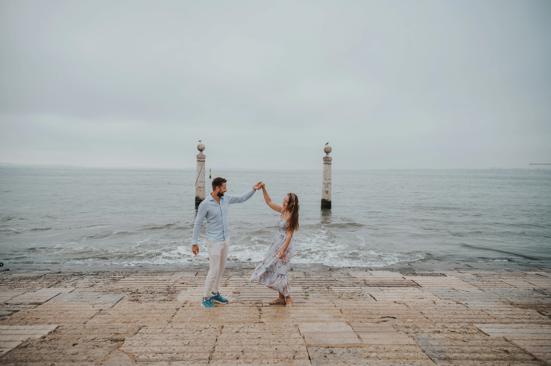 A turn beside the waterfront waves | Lisbon couple photoshoot The couple raising their joined hands for a turn beside the waves near Praça do Comércio during their couple photoshoot in Lisbon.