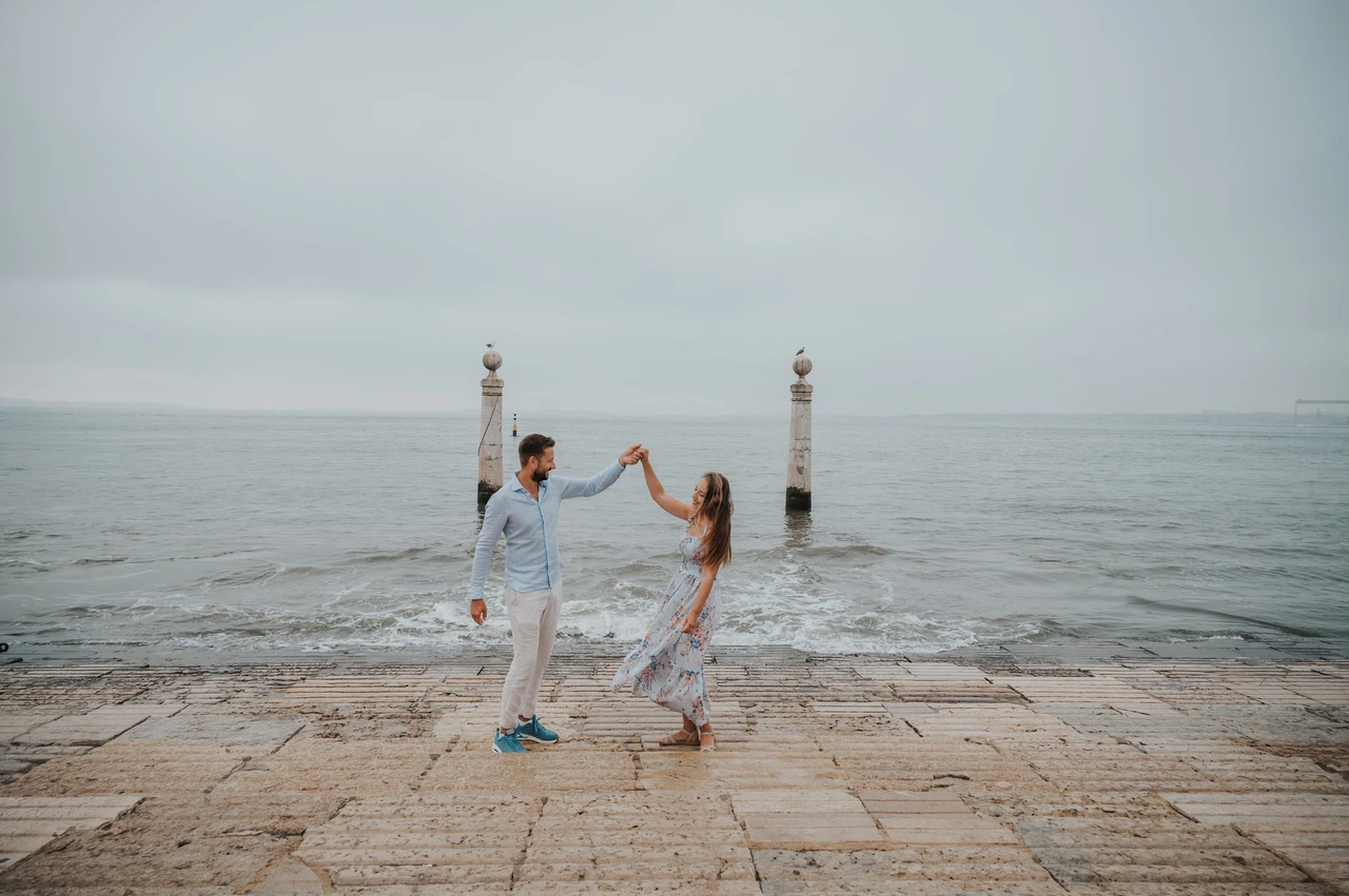 A turn beside the waterfront waves | Lisbon couple photoshoot The couple raising their joined hands for a turn beside the waves near Praça do Comércio during their couple photoshoot in Lisbon.