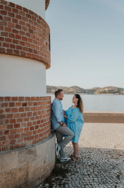 Together beside the curved waterfront wall | Lisbon engagement photoshoot The couple leaning close together beside a curved red-brick and white wall on the waterfront during their engagement photoshoot in Lisbon.